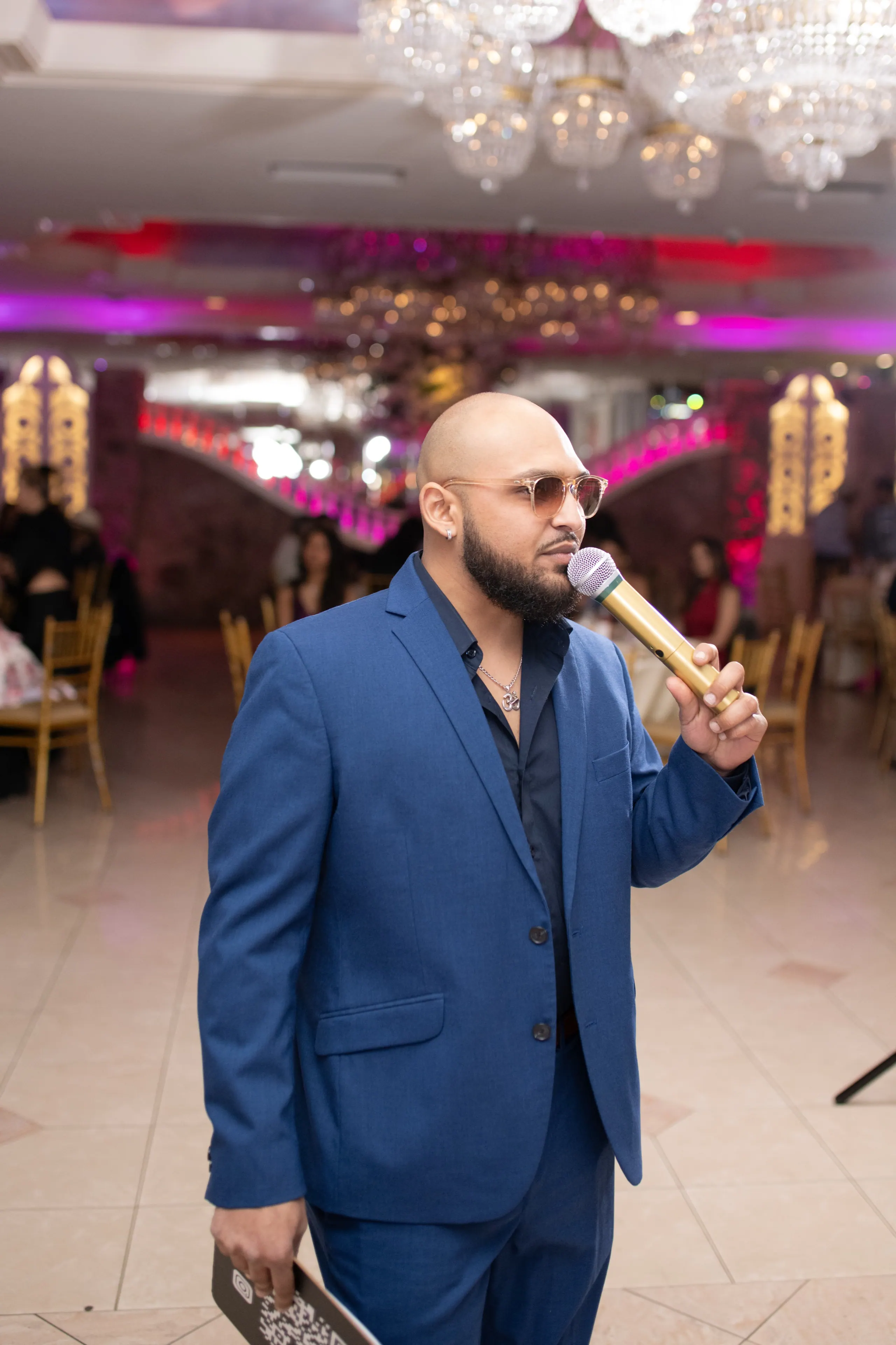 RAHH on the microphone in a blue suit under the chandeliers of a reception hall
