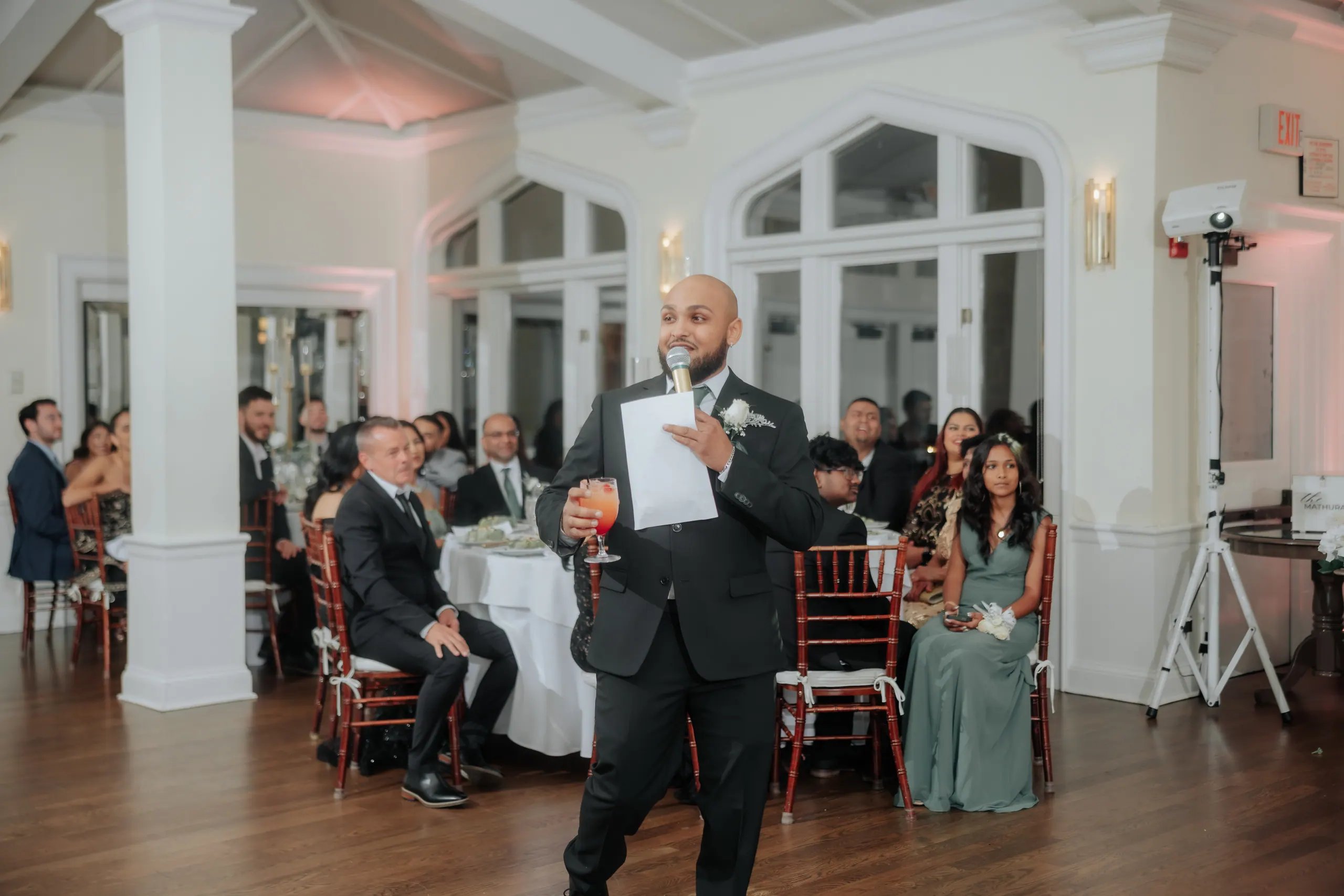 On the microphone during a wedding reception, seated guests watching