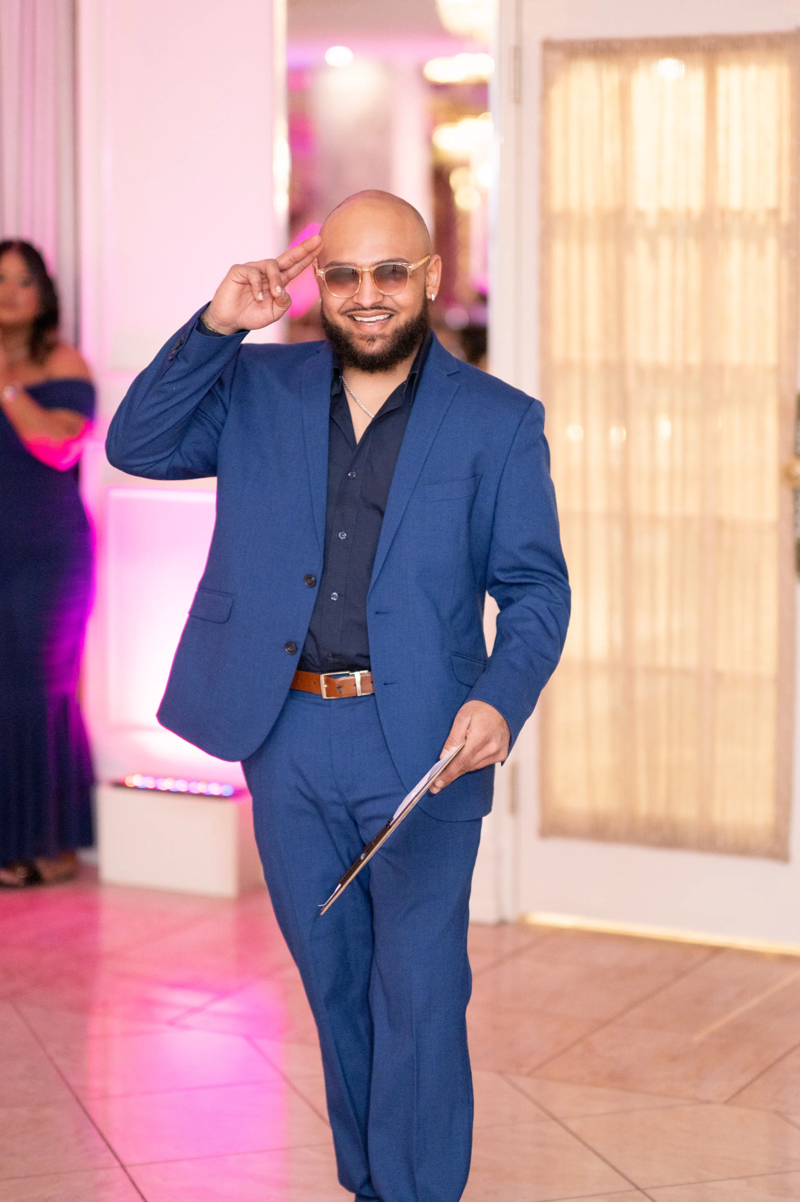 RAHH walking into a reception in a blue suit, mic cards in hand